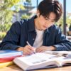 カフェのテラス席で語学テキストと単語カードを広げて書き取りをする男性