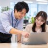 社内のIT窓口で同僚のノートパソコンの設定を手伝う男性社員