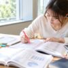 図書館の窓際で財務諸表の資料と電卓を広げて勉強する女性