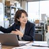 町工場の事務所でホワイトボードに業務の流れを描いて社長と話す女性コンサルタント