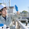 工場の排水処理設備で水質のサンプルを光にかざして確認する女性