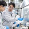 化学薬品の作業場で防護具をつけた主任が若い作業員に手順を教える場面