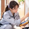 住宅の壁際で光回線の端末に配線をつなぎ測定器を確認する女性技術者