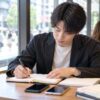 カフェでスマートフォン2台とノートを並べ面談の予定を書き込む男性